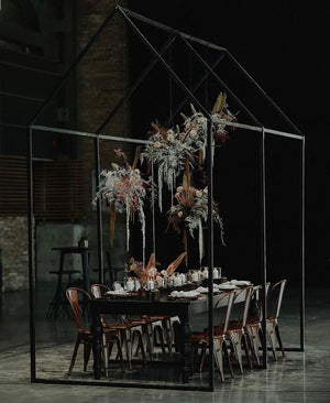 Dining table set under a glasshouse-like structure with decorative flowers and candles for an event in Vancouver